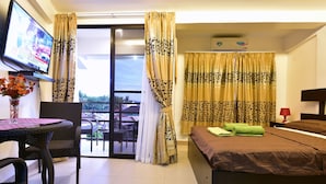 Habitación de hotel con cama, televisión, mesa con un florero y vistas al exterior.