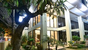 Un edificio moderno con un patio que tiene plantas en macetas, un banco de madera y un sendero de piedra.