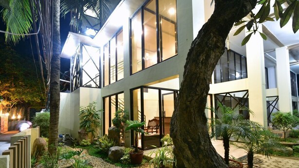 Un edificio moderno con grandes ventanales y un jardín cuidado con diversas plantas y un camino.