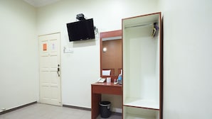 A hotel room with a desk, a television mounted on the wall, a door, and a trash bin. - Gurney Inn (George Town)