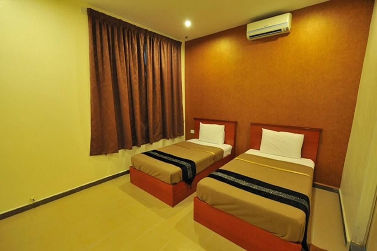 Quarto de hotel com duas camas, cortinas castanhas, ar condicionado fixado na parede e piso ladrilhado.