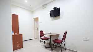 A small room with a wooden desk, two red chairs, a table, a flat-screen TV mounted on the wall, and a door leading to another room. - Gurney Inn (George Town)