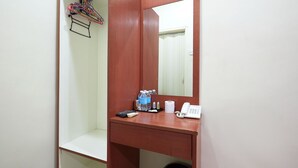 A hotel room with a wooden desk, a mirror, a telephone, a remote control, a bottle of water, and a small trash bin. - Gurney Inn (George Town)