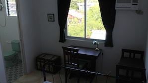 A small room with a window, a desk, a chair, a toilet, and an air conditioner. - Roger's Place Gay Guesthouse - Caters to Gay Men (Boracay Island)