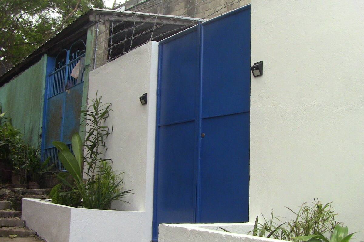 Un bâtiment avec une porte bleue et des murs blancs, entouré de verdure.