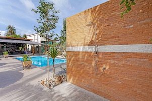 Zona de piscina con pared de ladrillo, ducha metálica y plantas en macetas.