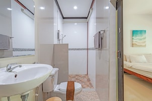 Un baño con lavamanos, inodoro y ducha blancos. Hay una toalla colgada en la pared y un cuadro en la pared contigua.