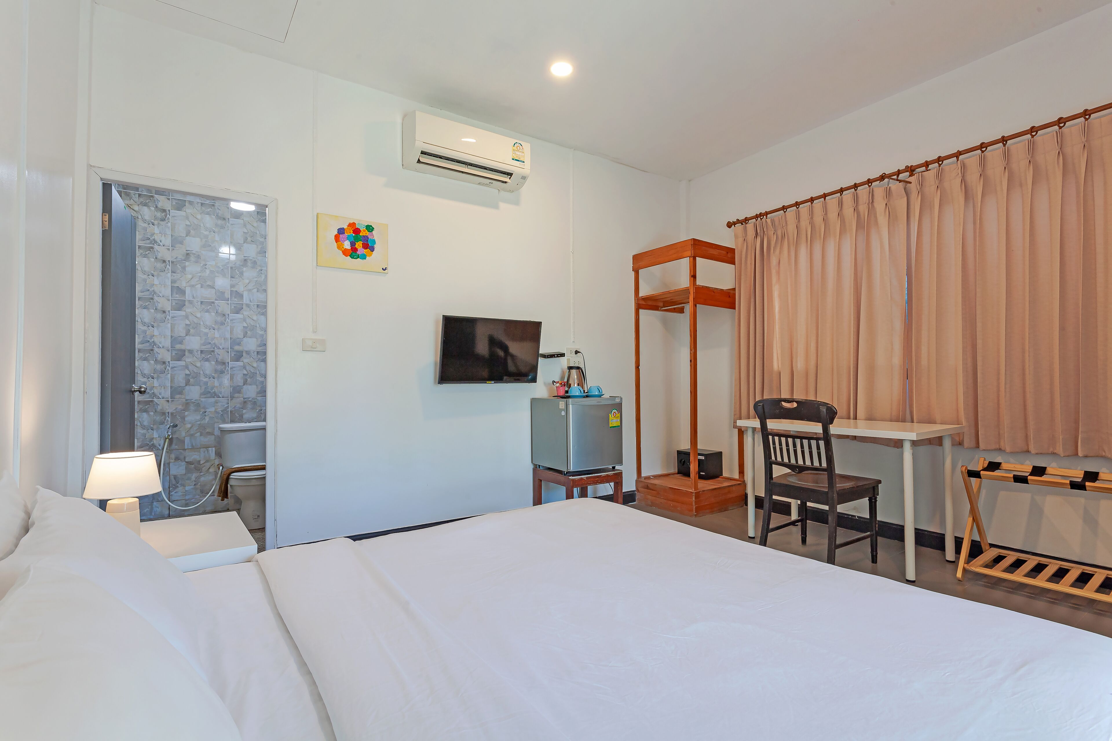 Une chambre d’hôtel équipée d’un lit, d’un bureau, d’une chaise, d’une télévision, d’un climatiseur et d’un espace douche.