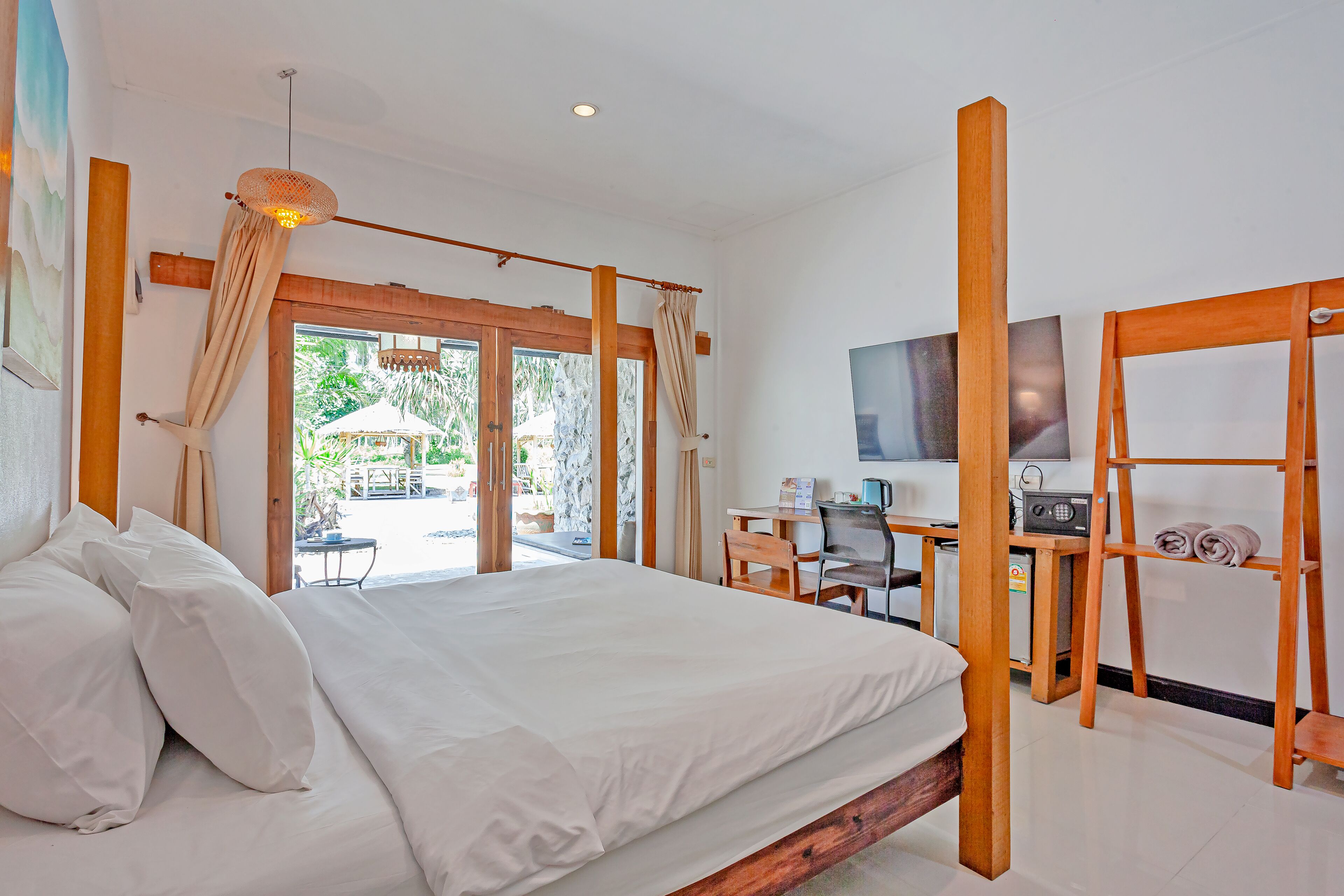 A bedroom with a bed, a desk, a chair, a television, and a view of the outdoors.