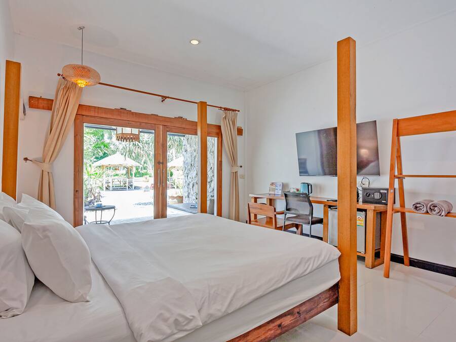 A bedroom with a bed, a desk, a chair, a television, and a view of the outdoors.