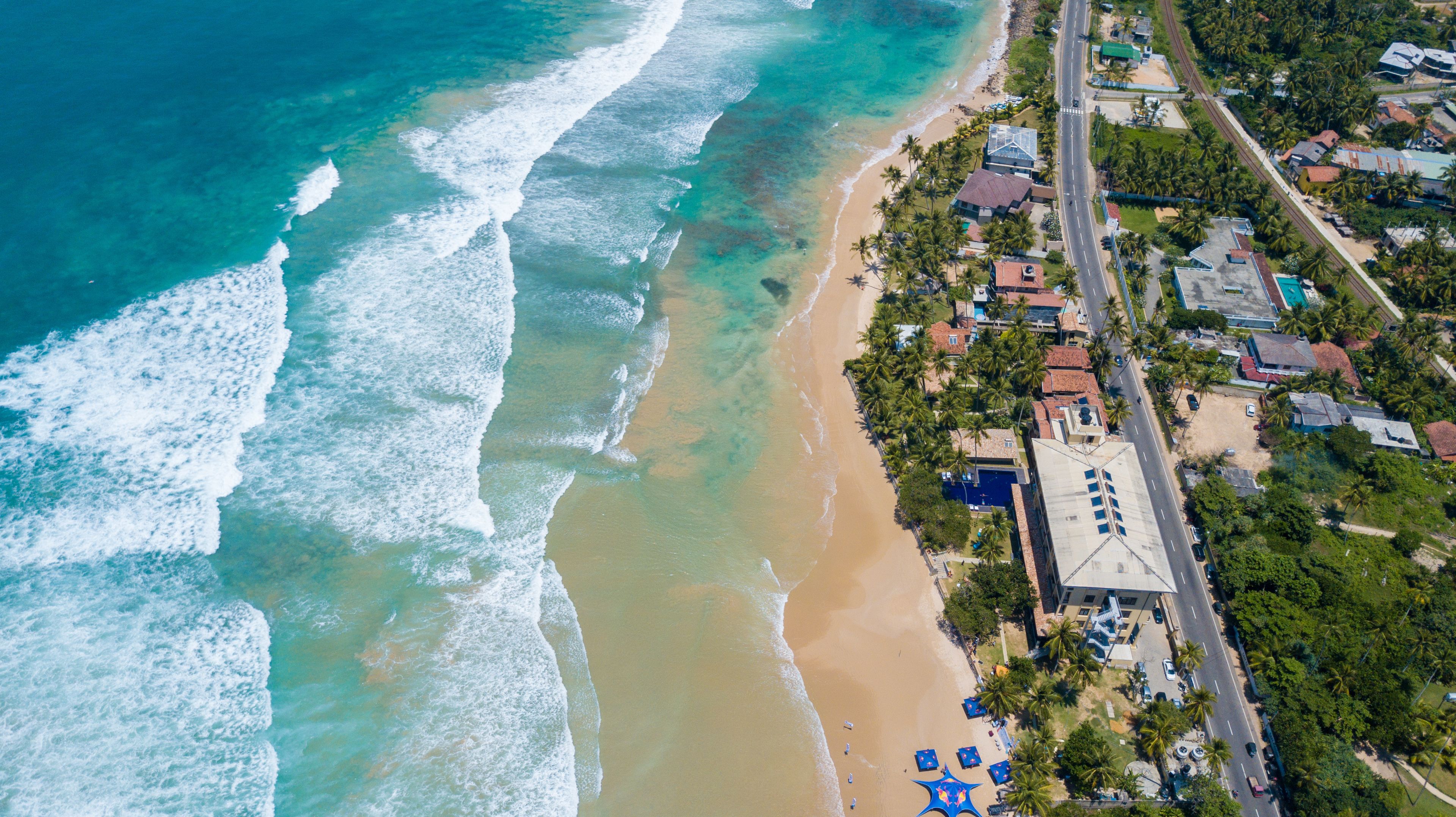 An aerial view of a coastal area with a beach, houses, and a road.