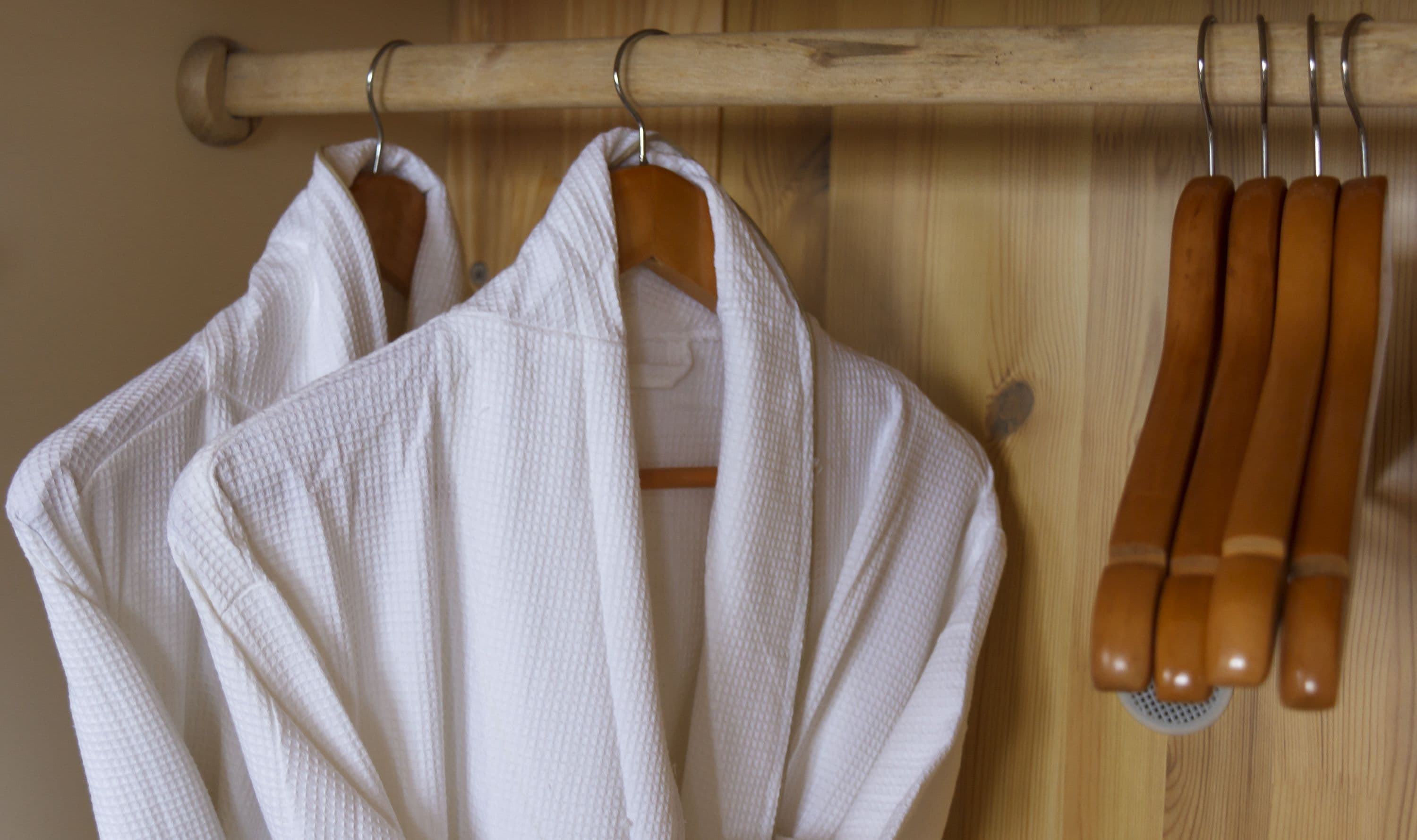 Two white bathrobes hanging on a wooden rack with wooden handles.
