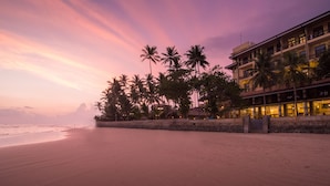 Un hotel frente a la playa con una hilera de palmeras y una playa al fondo.