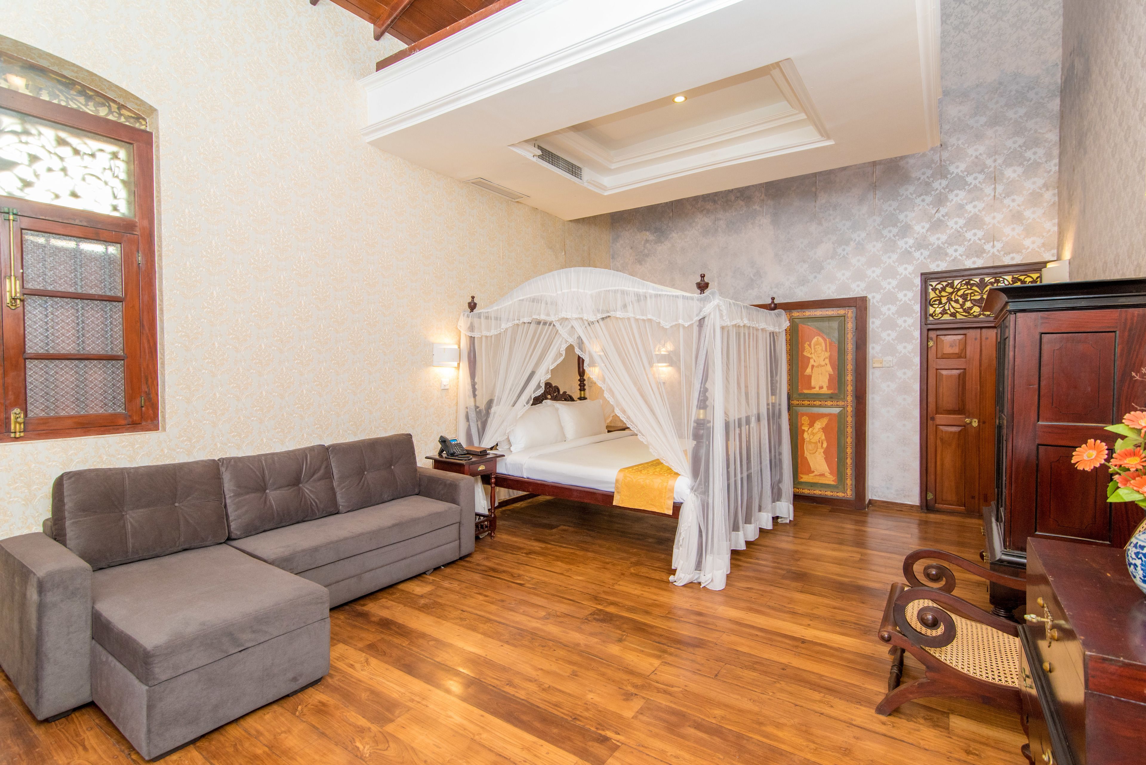 Una camera da letto con un letto a baldacchino, un divano grigio, pavimento in legno e un armadio in legno tradizionale.