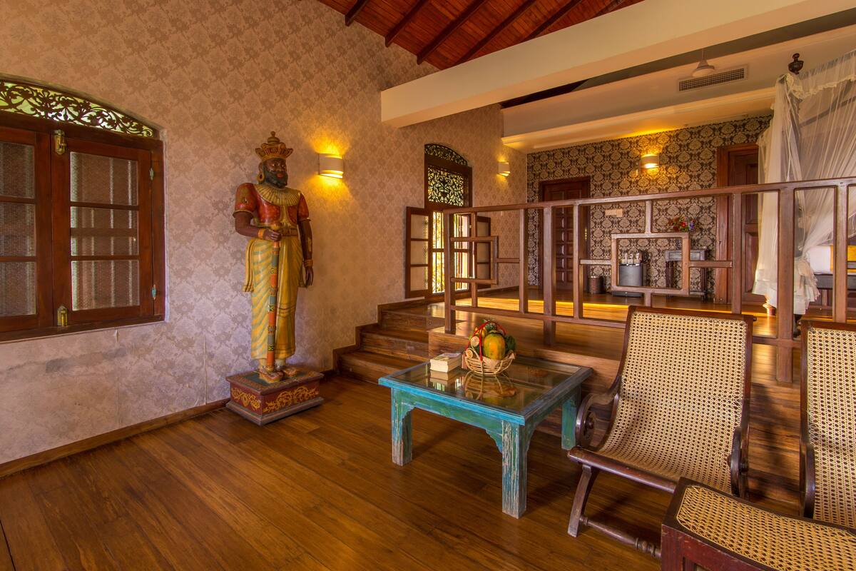 A traditional interior with wooden floors, a statue, a rattan chair, and a blue table.
