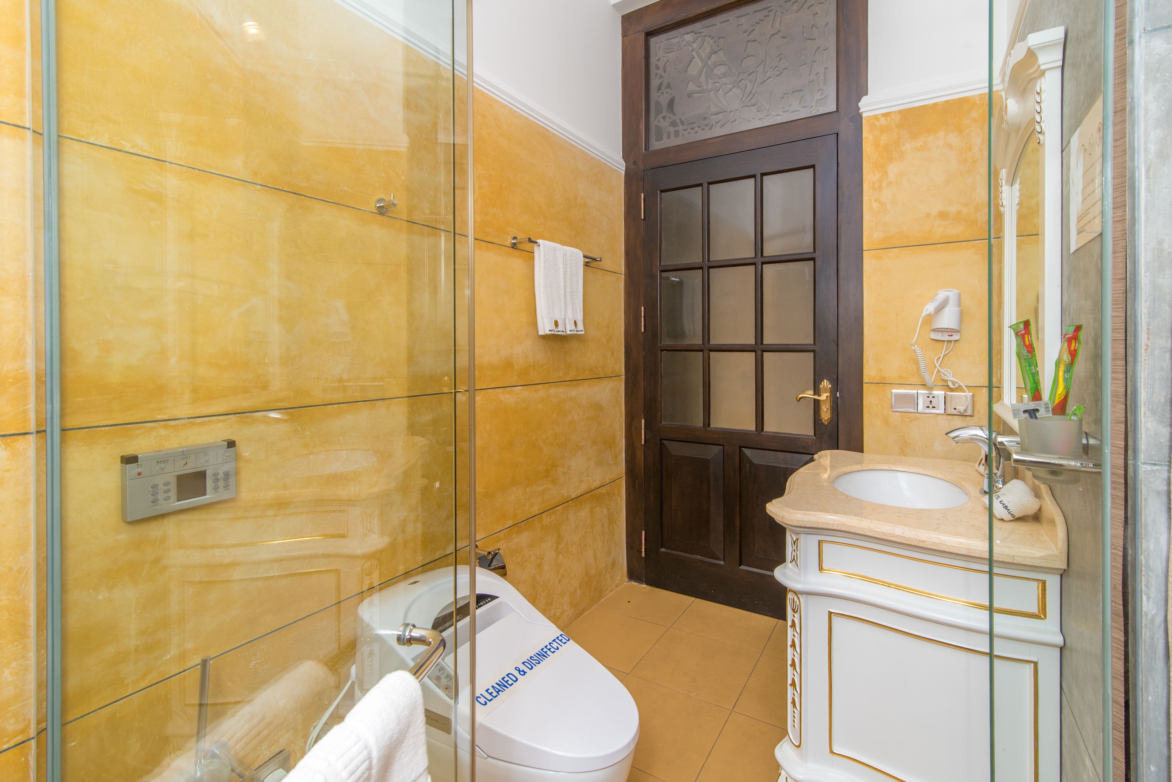 Un baño con cabina de ducha de vidrio, inodoro blanco, lavamanos color beige y puerta de madera.