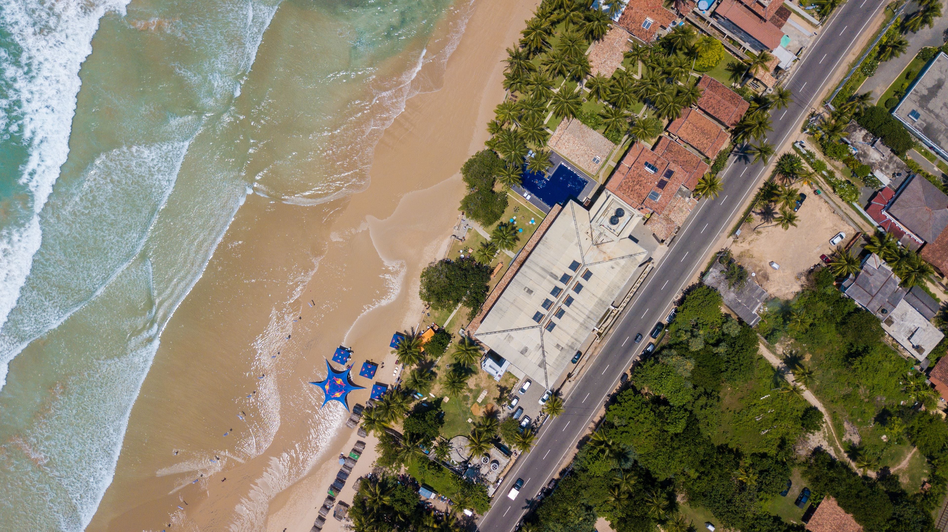 An aerial view of a beachside property with a large building, a road, and a beach.