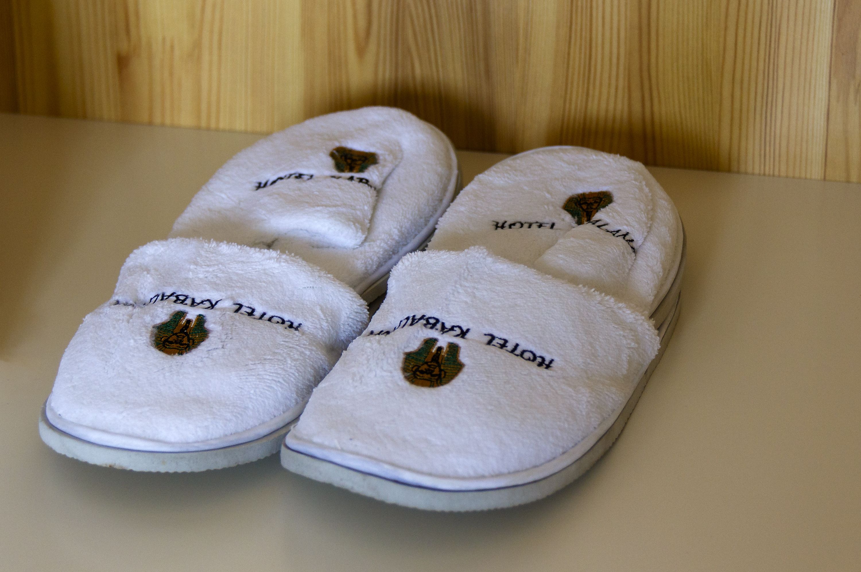A pair of white slippers with embroidered text and logos.
