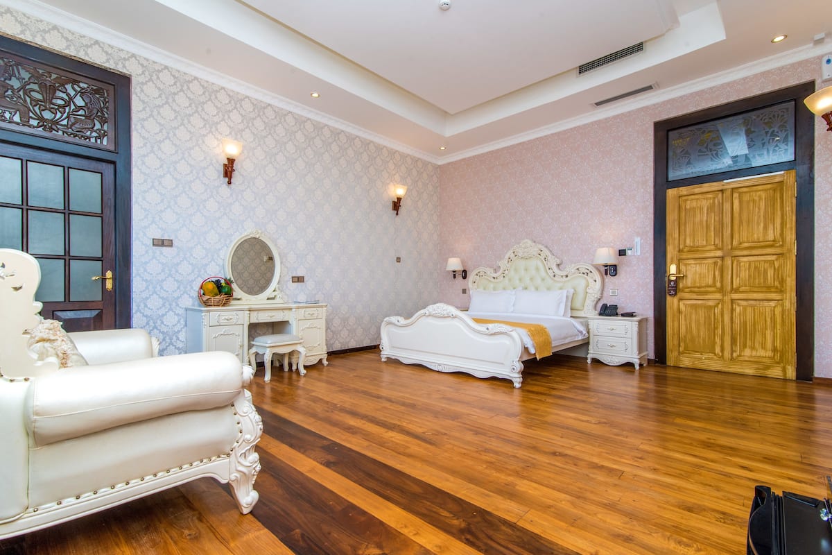 A spacious bedroom with a large bed, a sitting area with a chair, a desk, and a wardrobe.