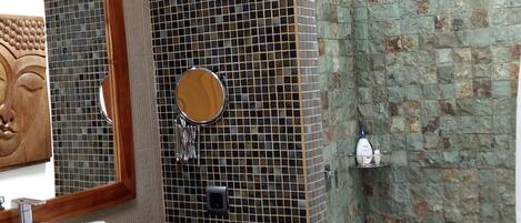 A bathroom with a white sink, a wooden-framed mirror, a round mirror, and a shower area with a stone wall.