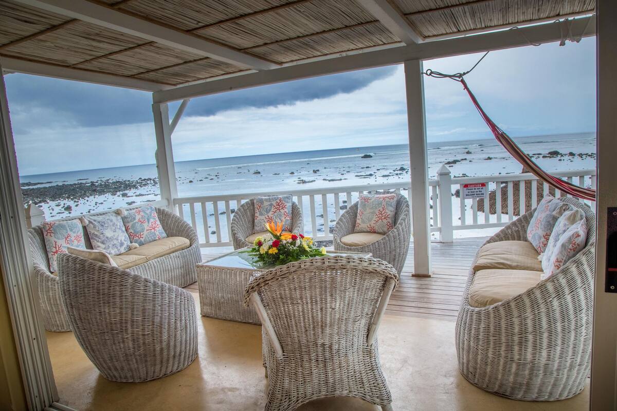 A covered outdoor seating area with wicker furniture and a view of the beach.