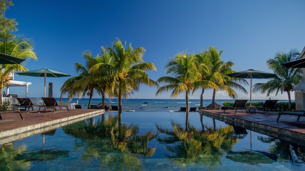 A clear pool with palm trees and lounge chairs, a view of the ocean, and a clear sky. - White Oaks Villas (Pointe Aux Piments)
