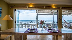 A dining area with a view of the beach, a table set with plates and cutlery, and a vase with flowers. - White Oaks Villas (Pointe Aux Piments)