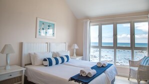 A bedroom with a large bed, two bedside tables, a window with a beach view, and a chair. - White Oaks Villas (Pointe Aux Piments)