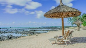A beach with a thatched umbrella, lounge chairs, and a rocky shoreline. - White Oaks Villas (Pointe Aux Piments)