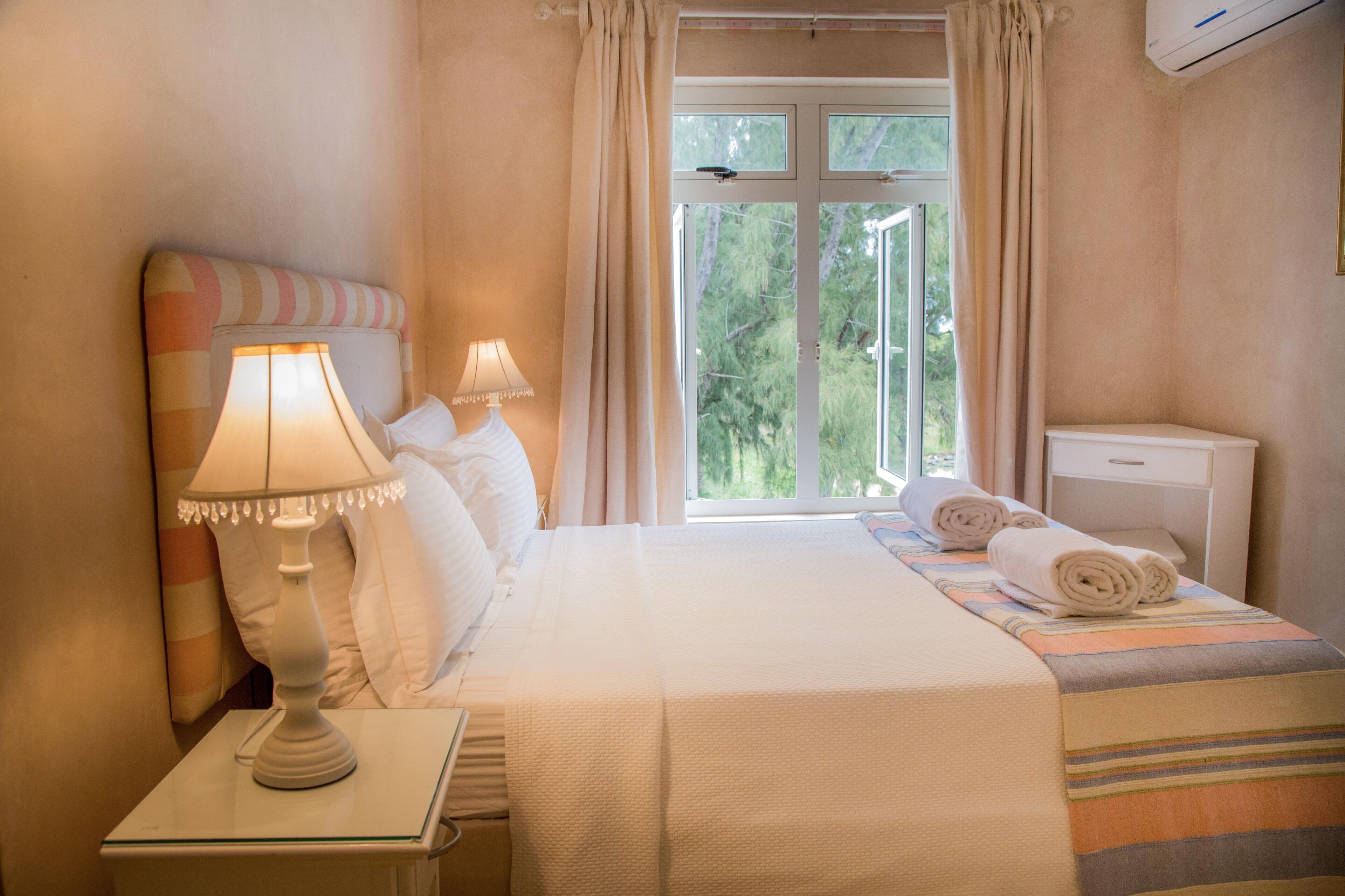 A hotel room with a bed, two bedside lamps, a window with curtains, a bedside table, and a small nightstand.