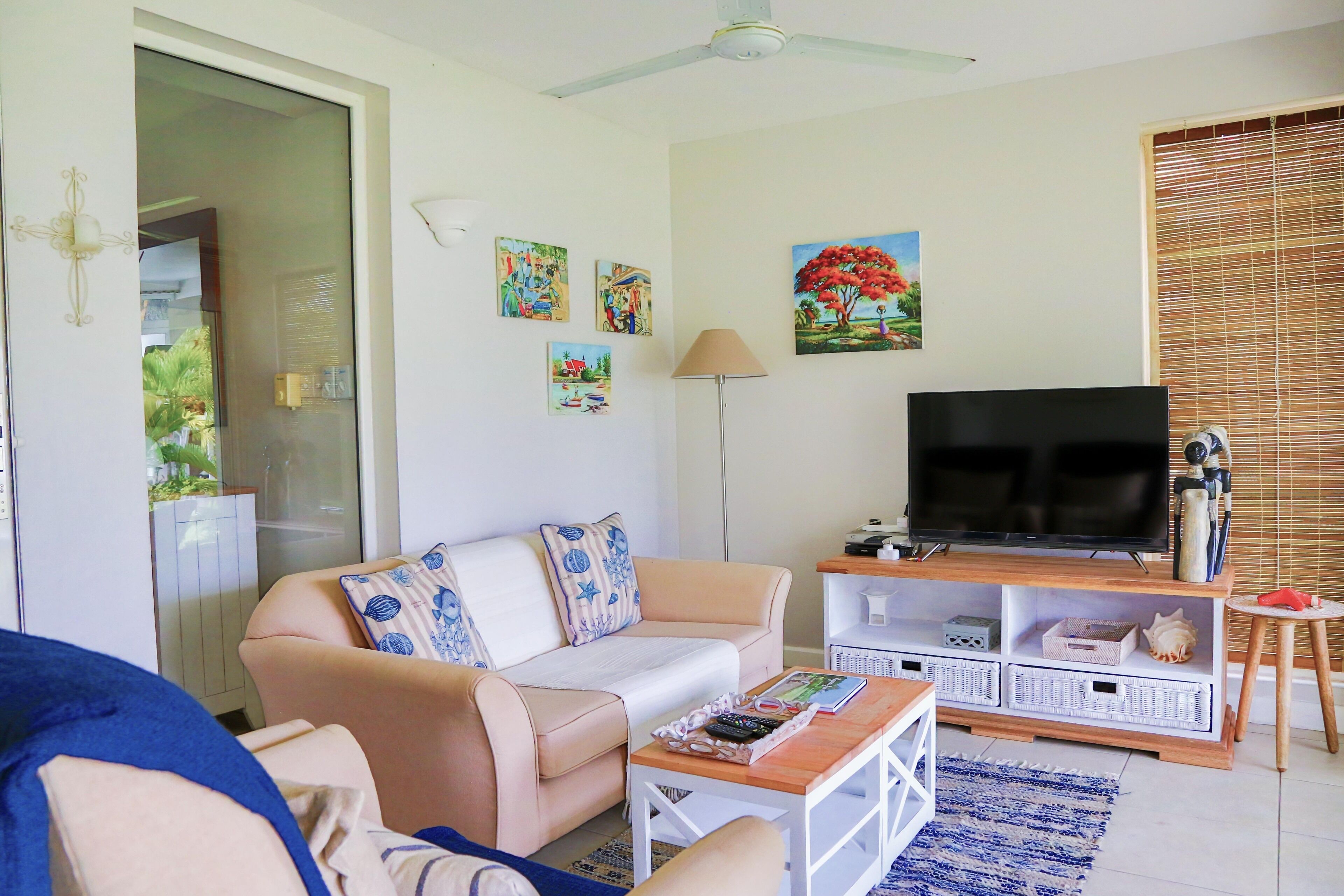 A living room with a beige sofa, a coffee table, a TV on a wooden stand, and a window with blinds.