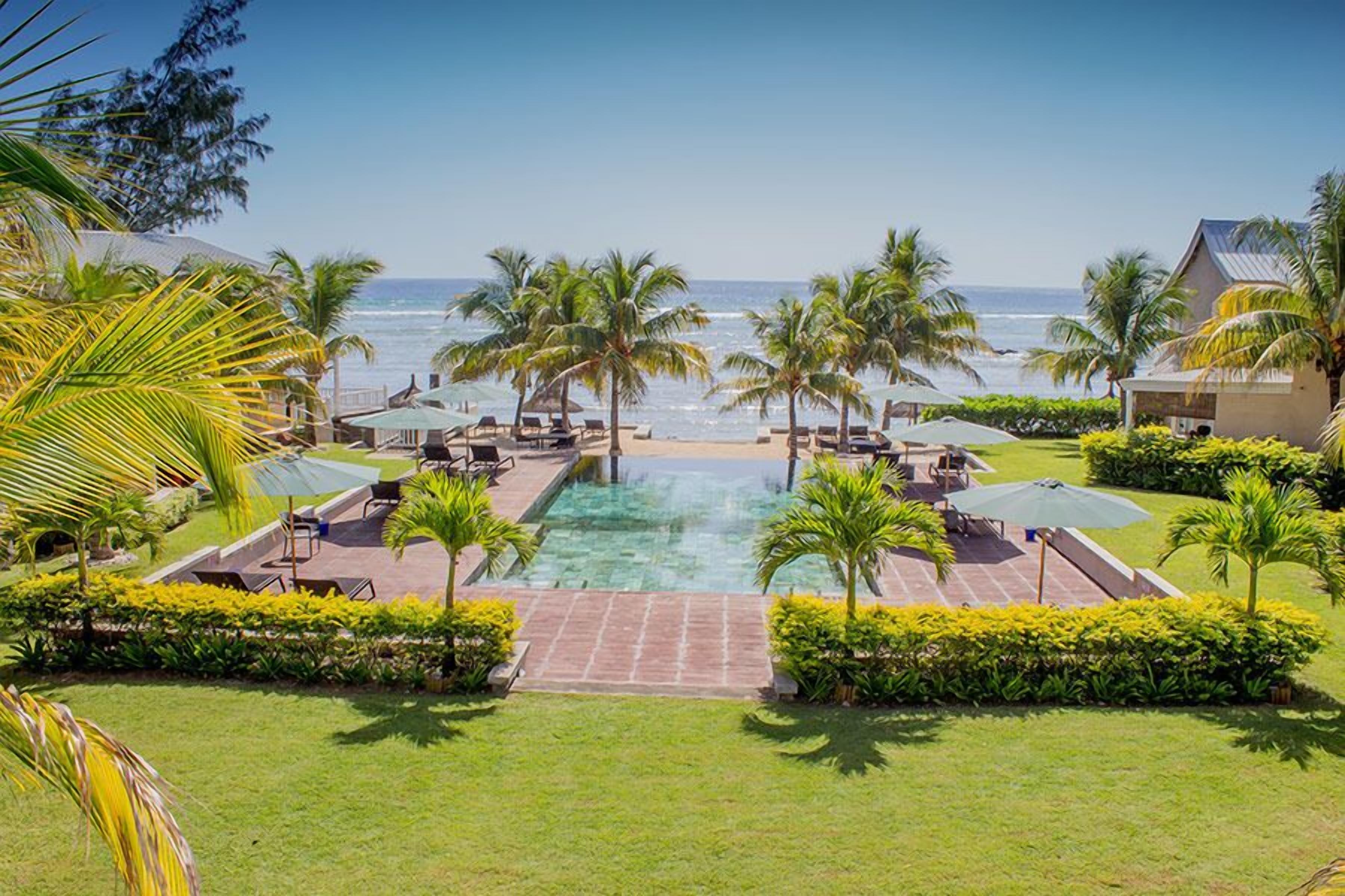 A resort with a pool, palm trees, and a view of the ocean.