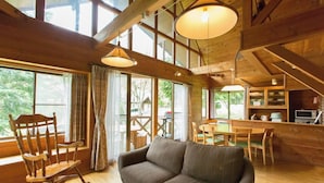 A cozy cabin interior with a sofa, rocking chair, dining table, and kitchen area.