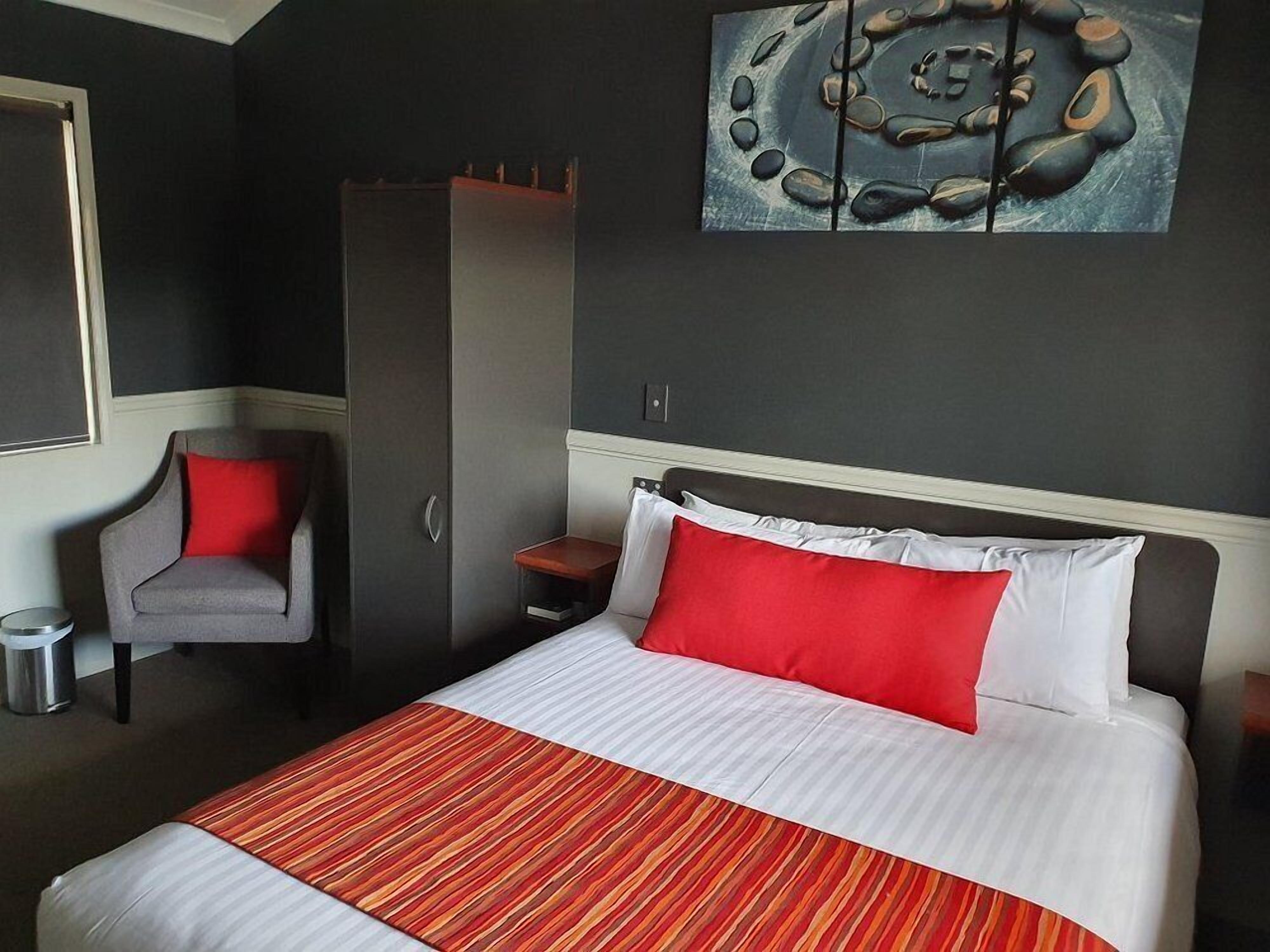 Quarto de hotel bem arrumado, com uma cama grande, uma cadeira, um guarda-roupa e um quadro na parede.