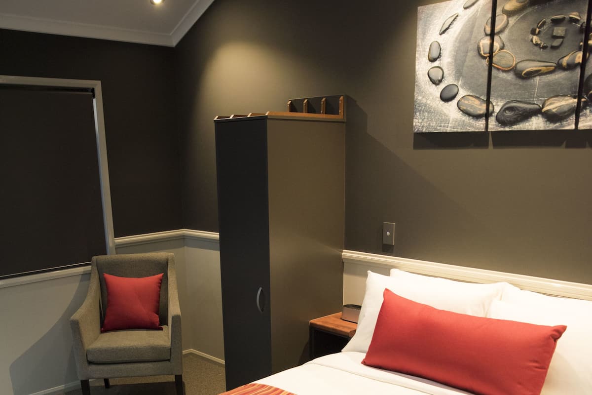 Une chambre d’hôtel bien aménagée, avec un grand lit, une chaise, une armoire et une œuvre d’art murale.