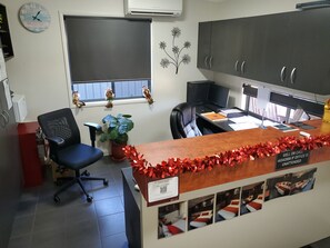 A reception desk with a QR code, a potted plant, a clock, and a window with decorative items.