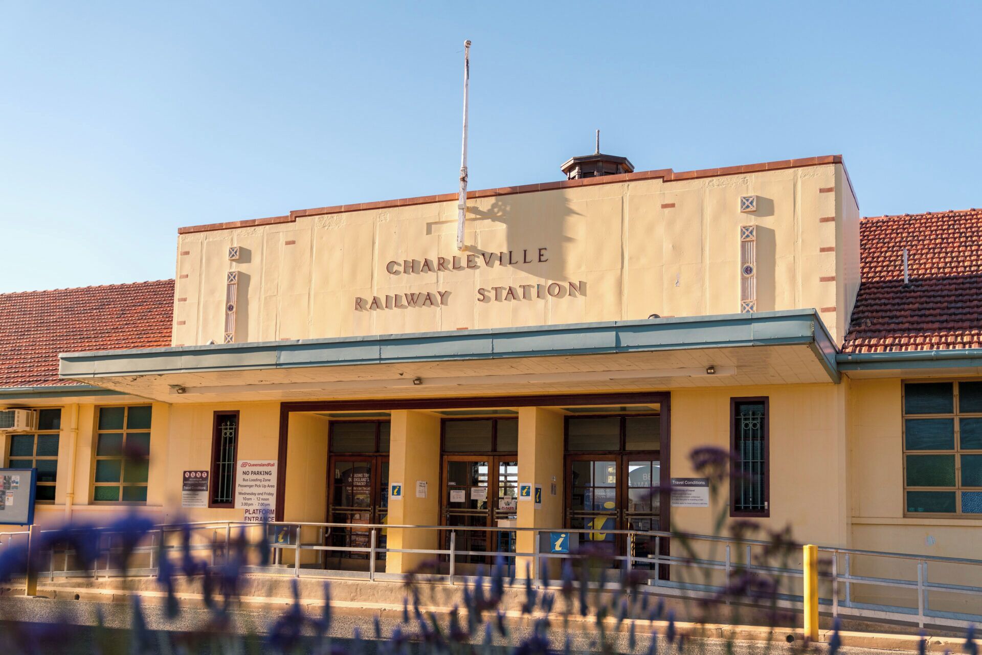 Un edificio con la indicación 'Charlleville Railway Station', con una entrada visible, señalización y un asta con bandera.