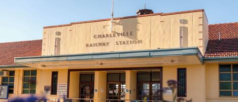 Un edificio con la indicación 'Charlleville Railway Station', con una entrada visible, señalización y un asta con bandera.
