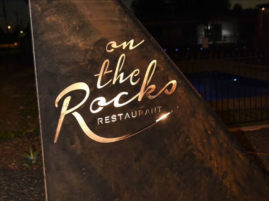 A sign for 'on the Rocks Restaurant' with a metallic finish and a reflective surface.