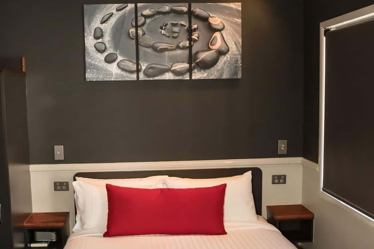 Une chambre d’hôtel avec un lit, une couvre-lit à rayures rouges et blanches, un oreiller rouge et une œuvre d’art murale au-dessus du lit.