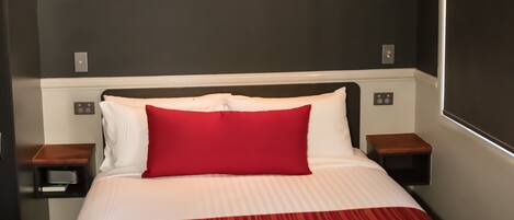 A hotel room with a bed, a red and white striped bedspread, a red pillow, and a painting on the wall.