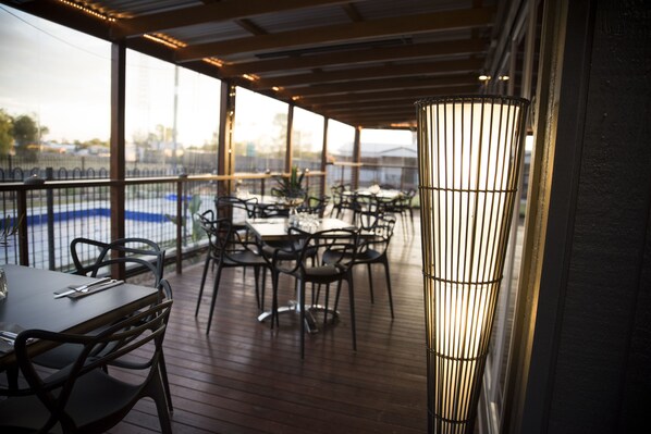 An outdoor dining area with tables and chairs, a railing, and a tall lamp post.