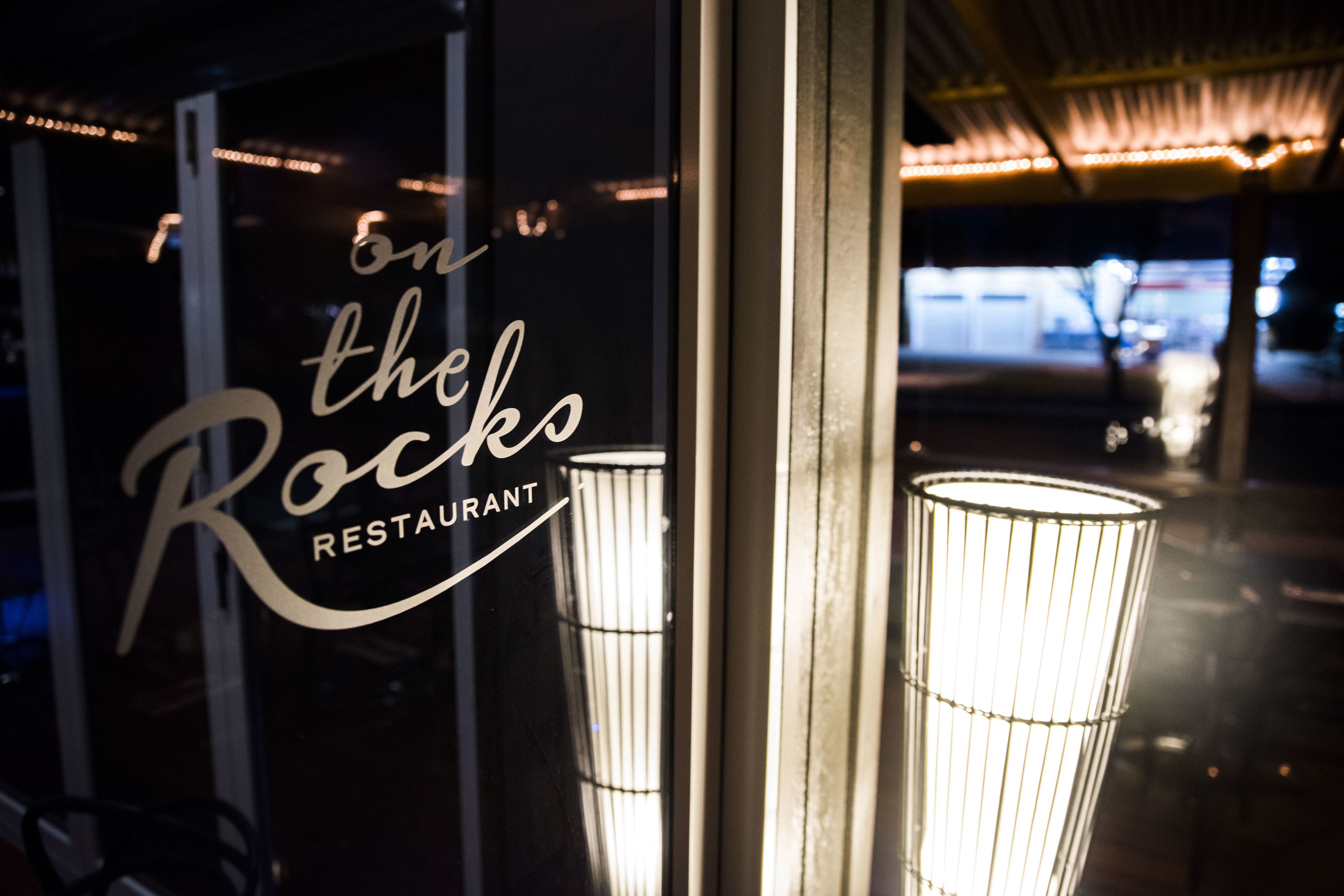 Letrero de restaurante con el nombre "On the Rocks" y un vidrio con una lámpara.