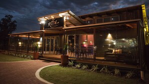 A modern restaurant with a glass facade, outdoor seating, and a sign that reads "On the Rocks Restaurant & Bar." - The Rocks Motel (Charleville)