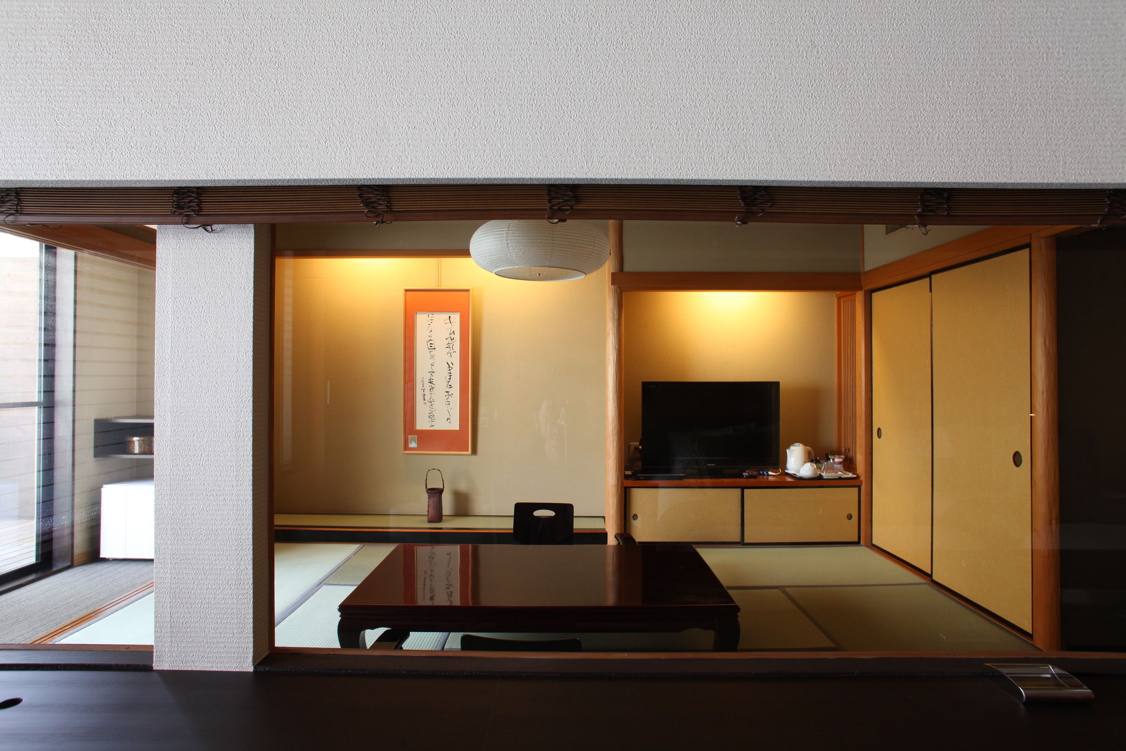 Ein traditioneller japanischer Raum mit Tatami-Boden, einem niedrigen Tisch, einem Fernseher und Schiebetüren.