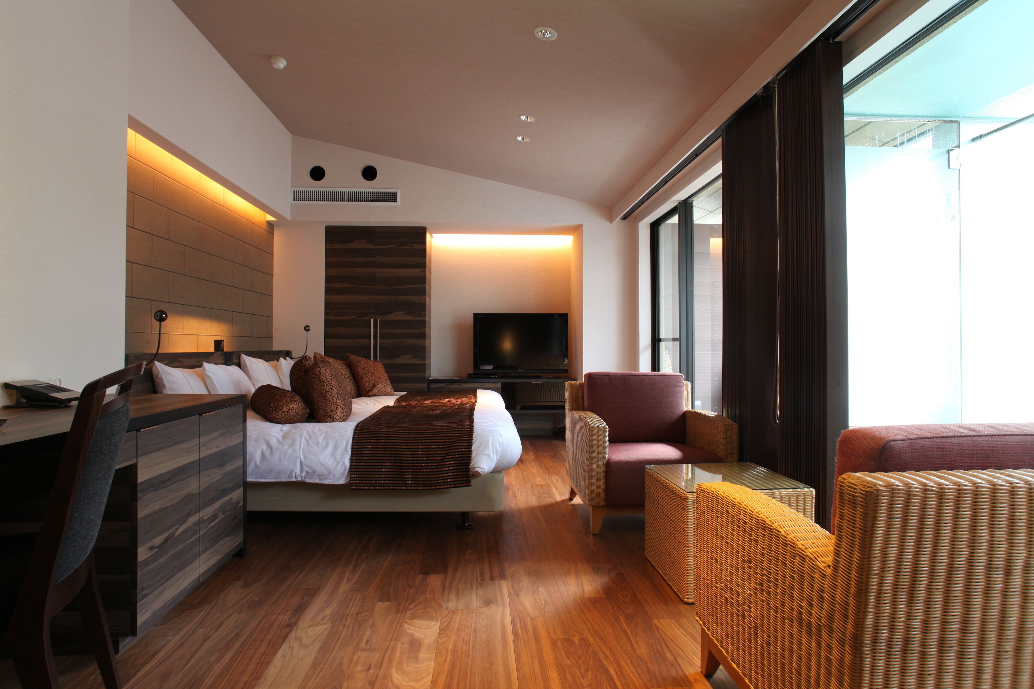 Quarto de hotel moderno com cama, escrivaninha, televisão e mobiliário de vime.