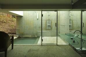 Un baño moderno con ducha envuelta en vidrio, lavamanos de vidrio y una pequeña zona de piscina.