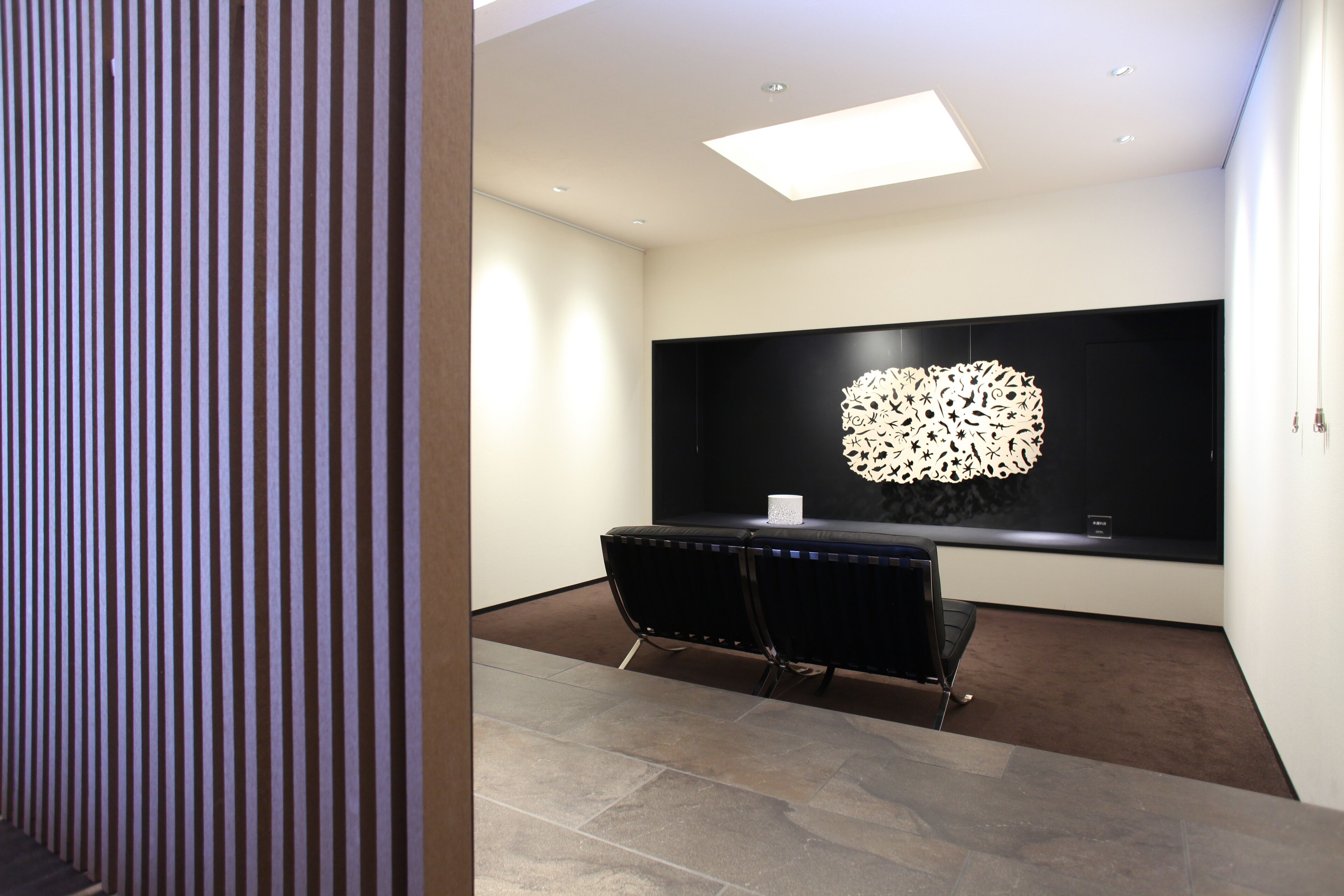 Un interior moderno con un banco tapizado en negro, una obra de arte mural geométrica e iluminación empotrada en el techo.
