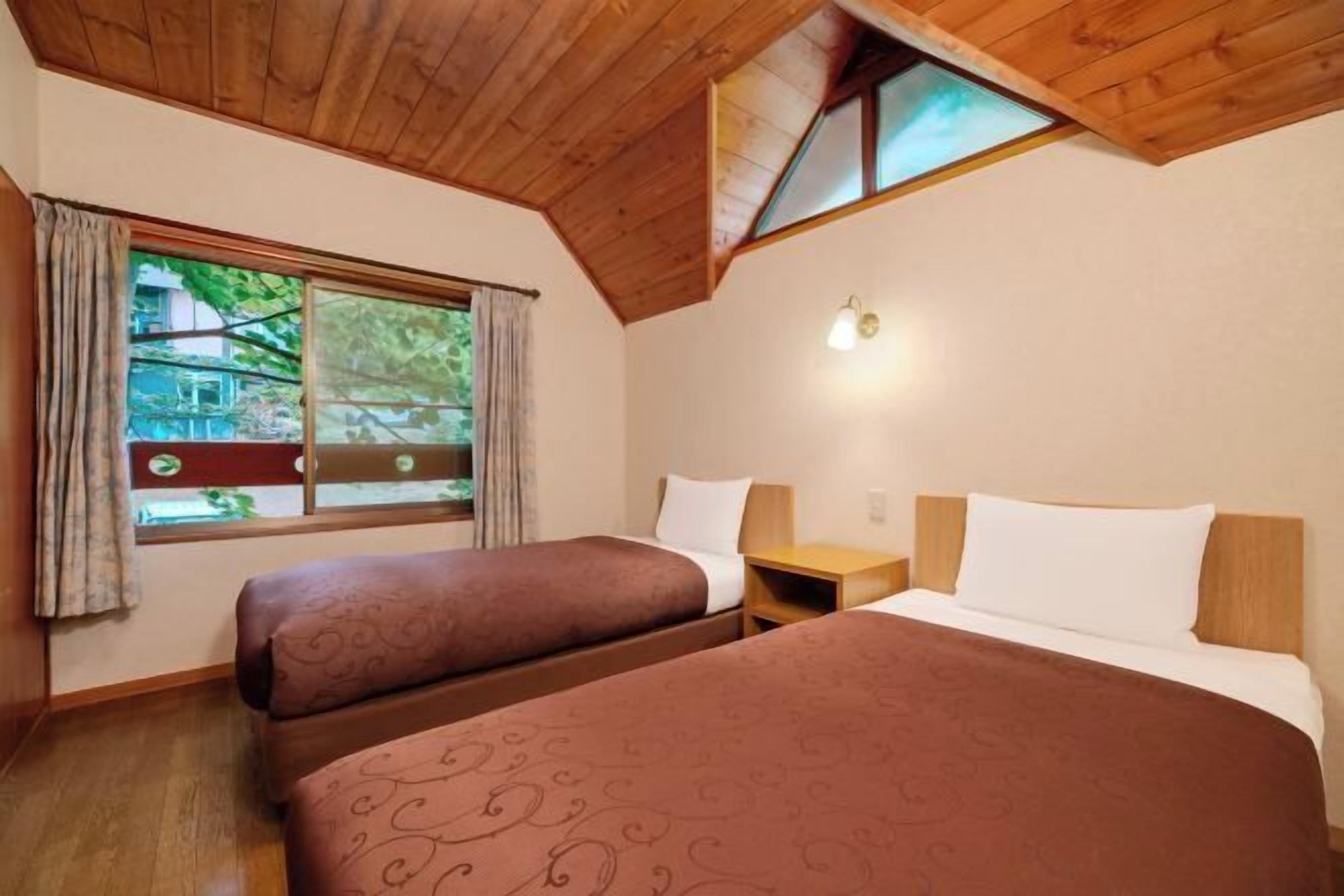 Une chambre avec deux lits, une fenêtre avec des rideaux, un plafond en bois et une table de chevet.