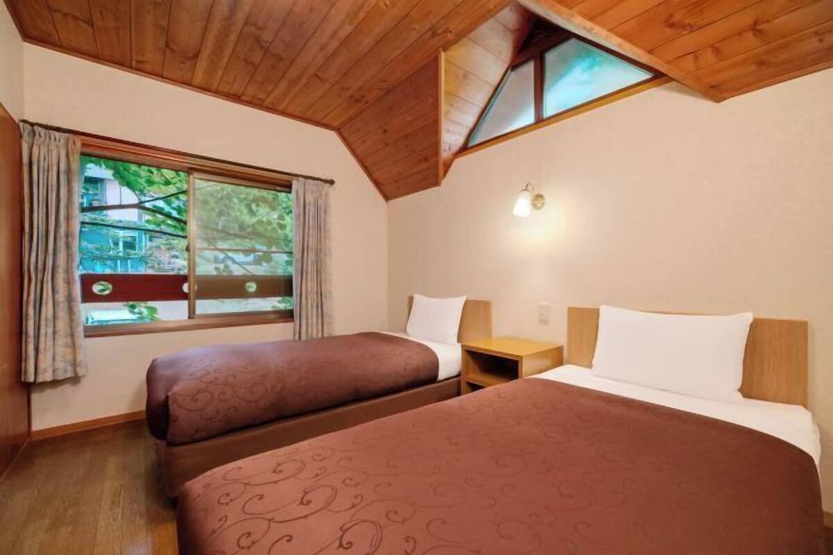 Une chambre avec deux lits, une fenêtre avec des rideaux, un plafond en bois et une table de chevet.